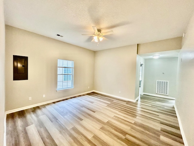 unfurnished room featuring a textured ceiling, electric panel, light hardwood / wood-style floors, and ceiling fan