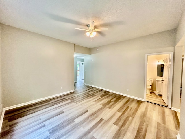 unfurnished bedroom with ensuite bathroom, light wood-type flooring, a textured ceiling, and ceiling fan