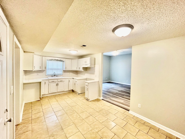 kitchen with white cabinets, a textured ceiling, sink, and light wood-type flooring