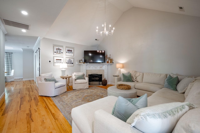 living room with hardwood / wood-style floors, a tiled fireplace, a notable chandelier, vaulted ceiling, and crown molding