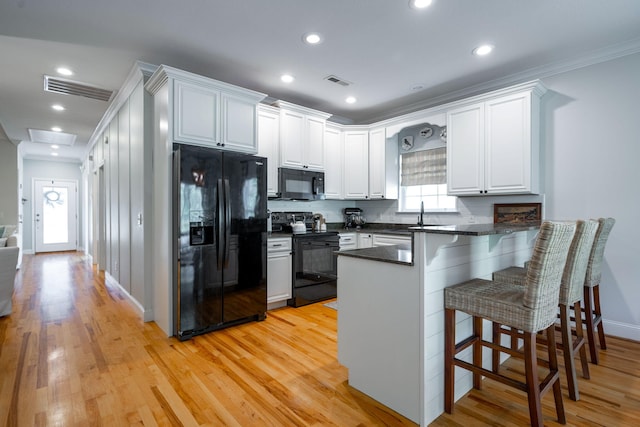 kitchen featuring white cabinetry, a kitchen bar, kitchen peninsula, crown molding, and black appliances