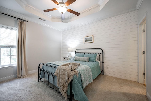 carpeted bedroom featuring ceiling fan, multiple windows, a tray ceiling, and ornamental molding