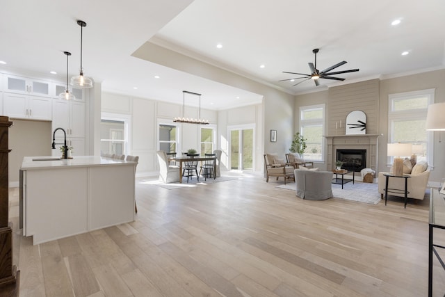 living room with a fireplace, light wood-type flooring, ceiling fan, and sink