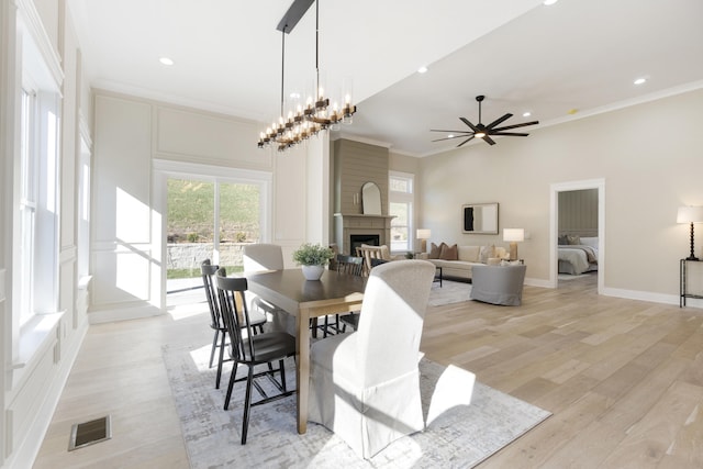 dining space featuring light wood-type flooring, ceiling fan with notable chandelier, a large fireplace, and ornamental molding