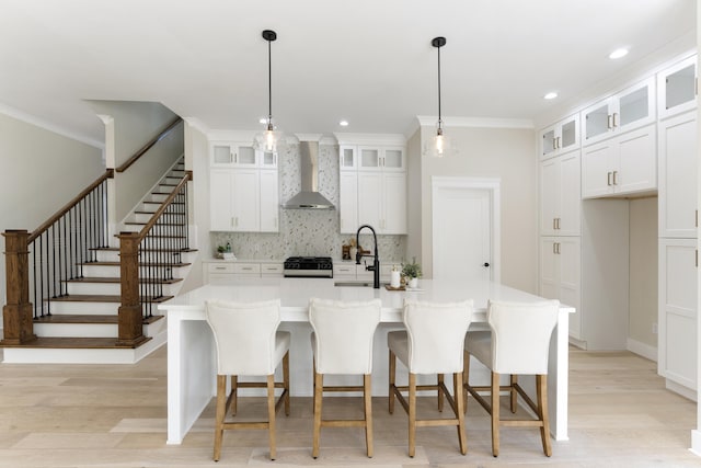 kitchen featuring gas range oven, sink, a center island with sink, and wall chimney range hood