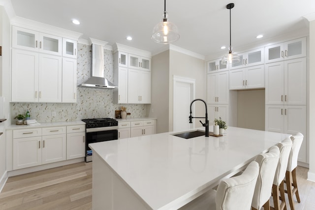 kitchen featuring a kitchen island with sink, sink, wall chimney range hood, white cabinets, and stainless steel range with gas cooktop