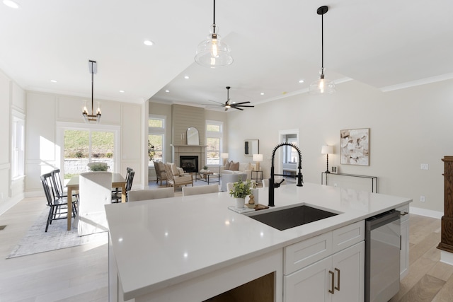 kitchen with white cabinets, decorative light fixtures, a center island with sink, and sink