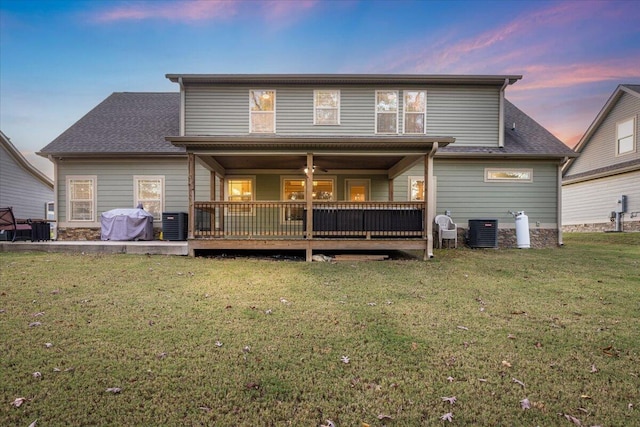 back house at dusk featuring central air condition unit, a wooden deck, and a lawn