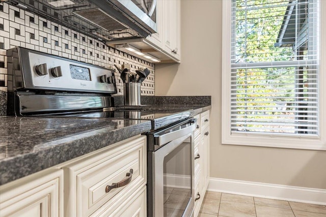 kitchen featuring decorative backsplash, light tile patterned floors, dark stone countertops, and electric stove