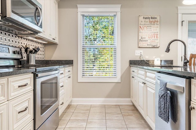 kitchen featuring sink, light tile patterned floors, dark stone counters, white cabinets, and appliances with stainless steel finishes