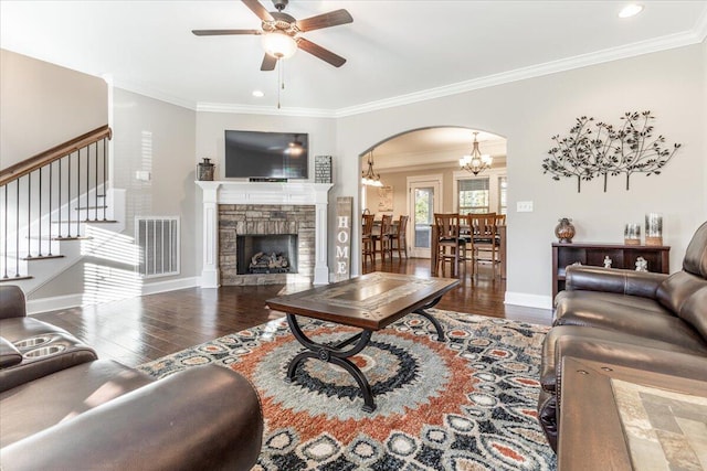 living room with ceiling fan with notable chandelier, a stone fireplace, dark hardwood / wood-style flooring, and ornamental molding