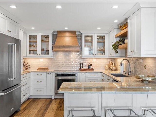 kitchen with kitchen peninsula, appliances with stainless steel finishes, custom range hood, and sink