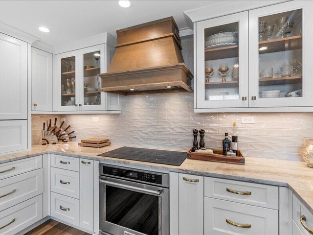 kitchen featuring white cabinetry, custom range hood, black electric cooktop, oven, and light stone counters