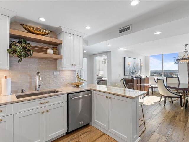 kitchen featuring dishwasher, sink, kitchen peninsula, white cabinets, and light wood-type flooring