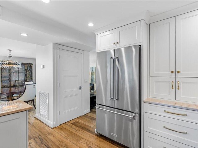 kitchen with light stone countertops, high end fridge, pendant lighting, light hardwood / wood-style flooring, and white cabinets