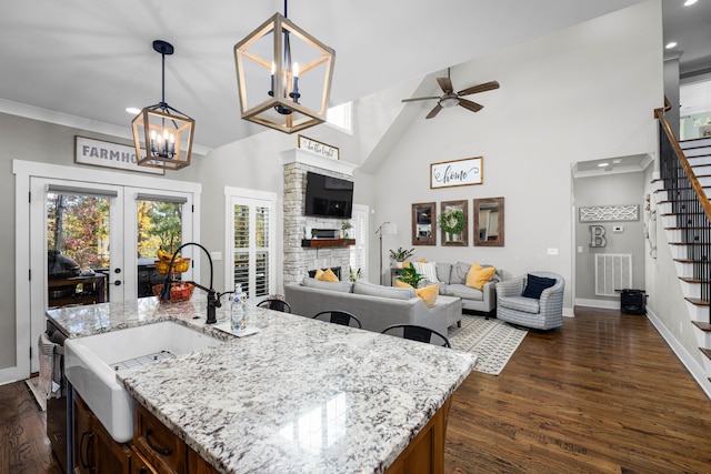 kitchen featuring light stone countertops, french doors, dark hardwood / wood-style flooring, hanging light fixtures, and an island with sink