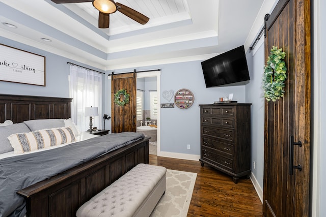 bedroom with ensuite bath, ceiling fan, a barn door, dark hardwood / wood-style floors, and a tray ceiling