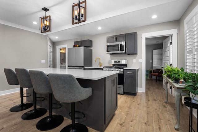 kitchen featuring gray cabinets, hanging light fixtures, appliances with stainless steel finishes, and light hardwood / wood-style flooring