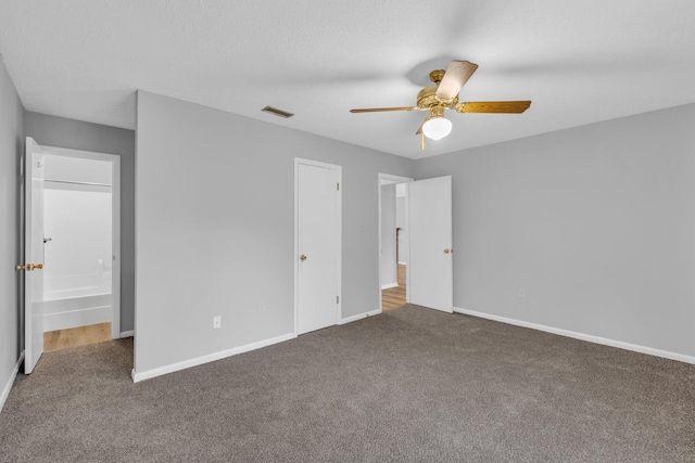 unfurnished bedroom featuring ceiling fan, carpet floors, a textured ceiling, and ensuite bath