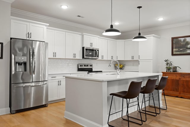 kitchen featuring white cabinets, decorative light fixtures, stainless steel appliances, and a center island with sink