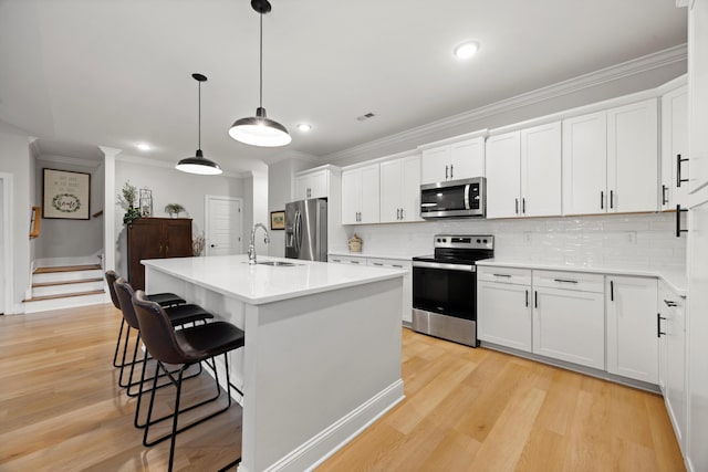 kitchen featuring appliances with stainless steel finishes, sink, pendant lighting, a center island with sink, and white cabinetry