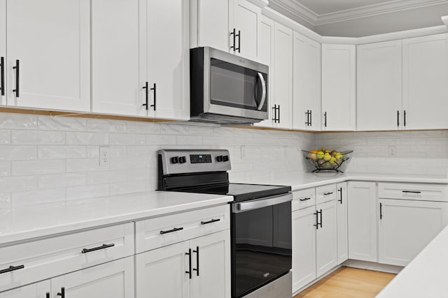 kitchen featuring decorative backsplash, white cabinetry, crown molding, and appliances with stainless steel finishes