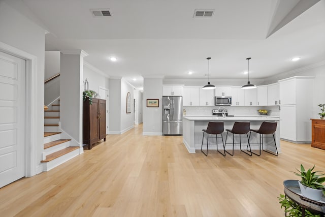 kitchen featuring backsplash, hanging light fixtures, light hardwood / wood-style flooring, an island with sink, and stainless steel appliances