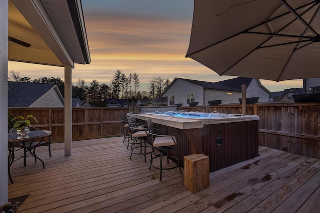 deck at dusk featuring a bar and a hot tub