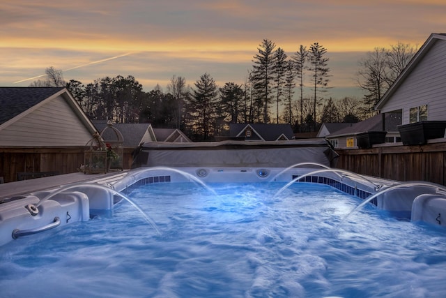 pool at dusk featuring pool water feature and a hot tub