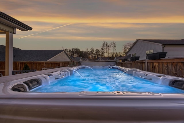 pool at dusk featuring pool water feature and a hot tub