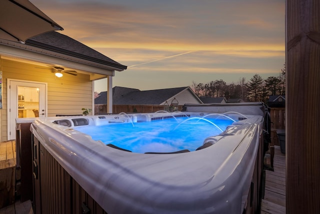 pool at dusk with a wooden deck and a hot tub