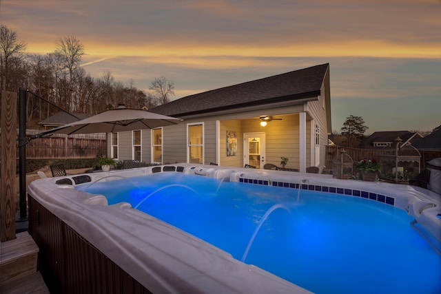 pool at dusk with ceiling fan and a hot tub