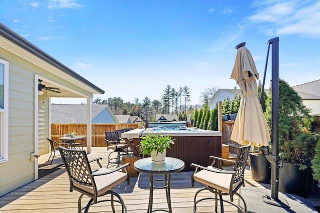 deck featuring a hot tub, fence, outdoor dining space, and ceiling fan