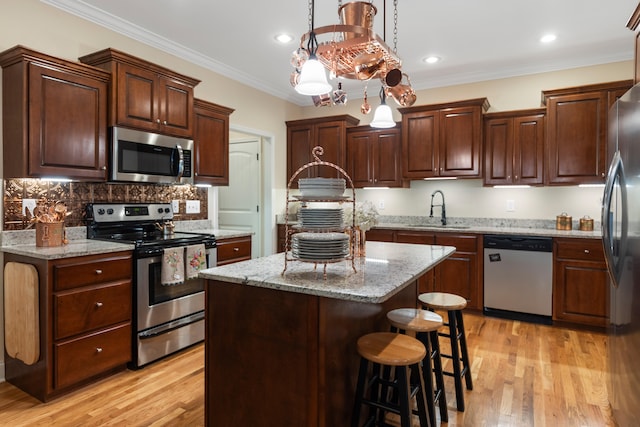 kitchen with a center island, light wood-type flooring, decorative light fixtures, appliances with stainless steel finishes, and ornamental molding