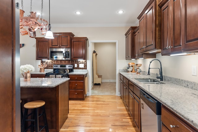 kitchen with appliances with stainless steel finishes, light wood-type flooring, ornamental molding, sink, and pendant lighting