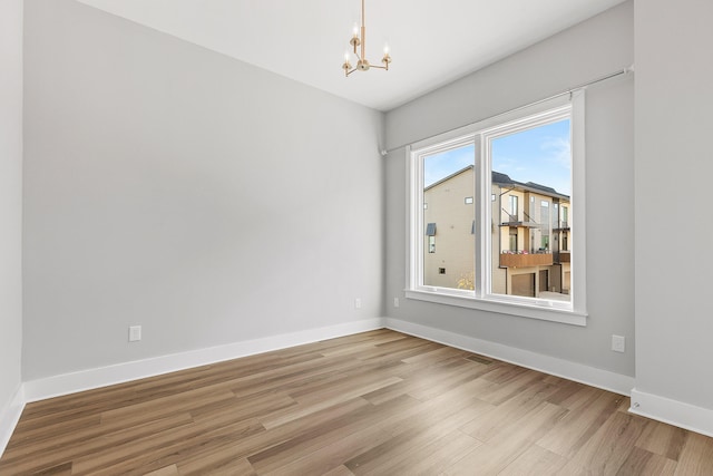 empty room featuring a healthy amount of sunlight, a notable chandelier, and light wood-type flooring