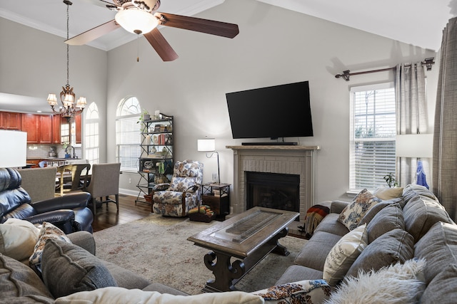 living room with high vaulted ceiling, hardwood / wood-style flooring, a fireplace, ceiling fan with notable chandelier, and ornamental molding