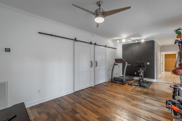 workout area with a barn door, hardwood / wood-style flooring, ceiling fan, and ornamental molding