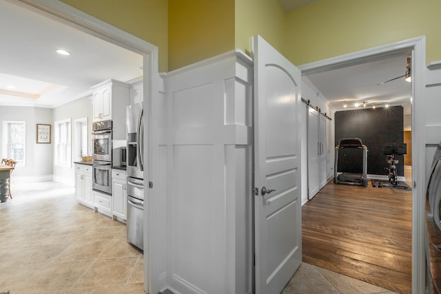 kitchen featuring light wood-type flooring, ornamental molding, stainless steel appliances, a barn door, and white cabinetry