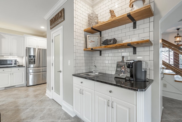 kitchen featuring white cabinets, decorative backsplash, ornamental molding, light tile patterned floors, and stainless steel appliances