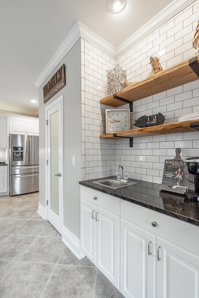 kitchen with stainless steel refrigerator with ice dispenser, tasteful backsplash, ornamental molding, light tile patterned floors, and white cabinetry