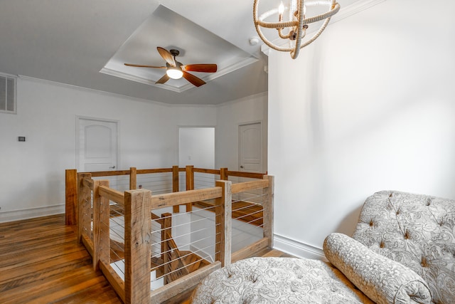 bedroom with wood-type flooring, ceiling fan with notable chandelier, a tray ceiling, and crown molding