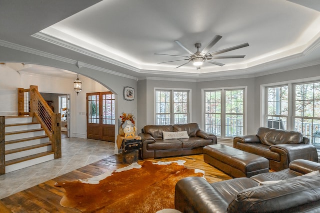 living room with a raised ceiling, ceiling fan, french doors, and ornamental molding