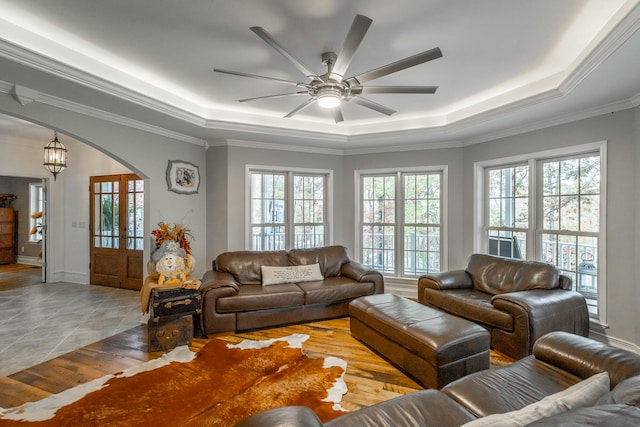 living room featuring a raised ceiling, a wealth of natural light, ornamental molding, and ceiling fan