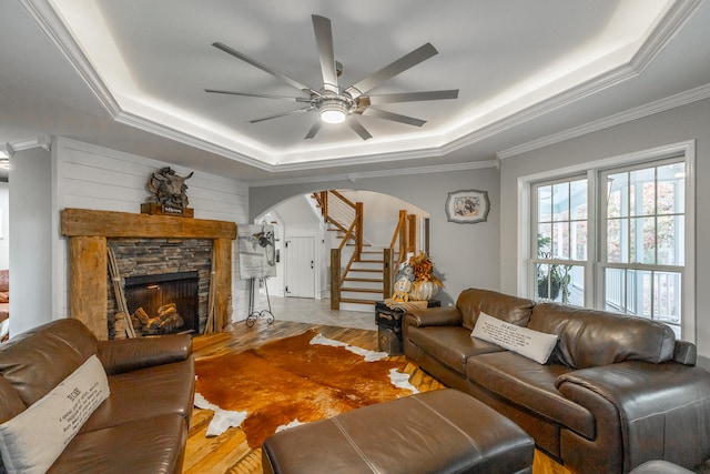 living room with a stone fireplace, a raised ceiling, and light wood-type flooring