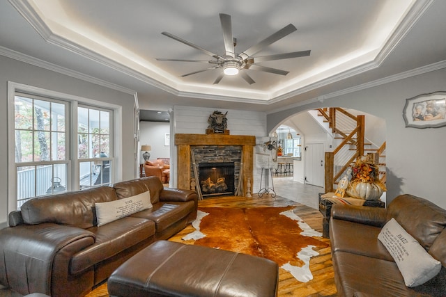 living room with a tray ceiling, ceiling fan, crown molding, hardwood / wood-style flooring, and a fireplace