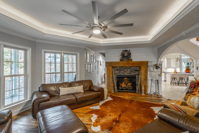 living room featuring a raised ceiling, ceiling fan, ornamental molding, a fireplace, and wood-type flooring