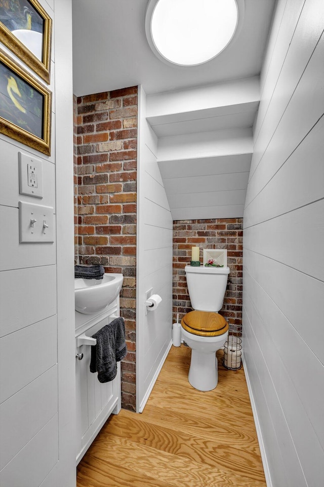 bathroom featuring hardwood / wood-style floors, toilet, and brick wall