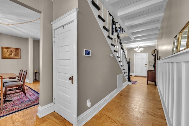 hallway featuring beam ceiling, light hardwood / wood-style flooring, and a chandelier