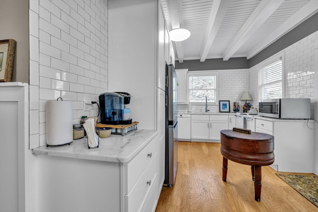 kitchen with decorative backsplash, appliances with stainless steel finishes, light stone countertops, white cabinets, and light hardwood / wood-style floors